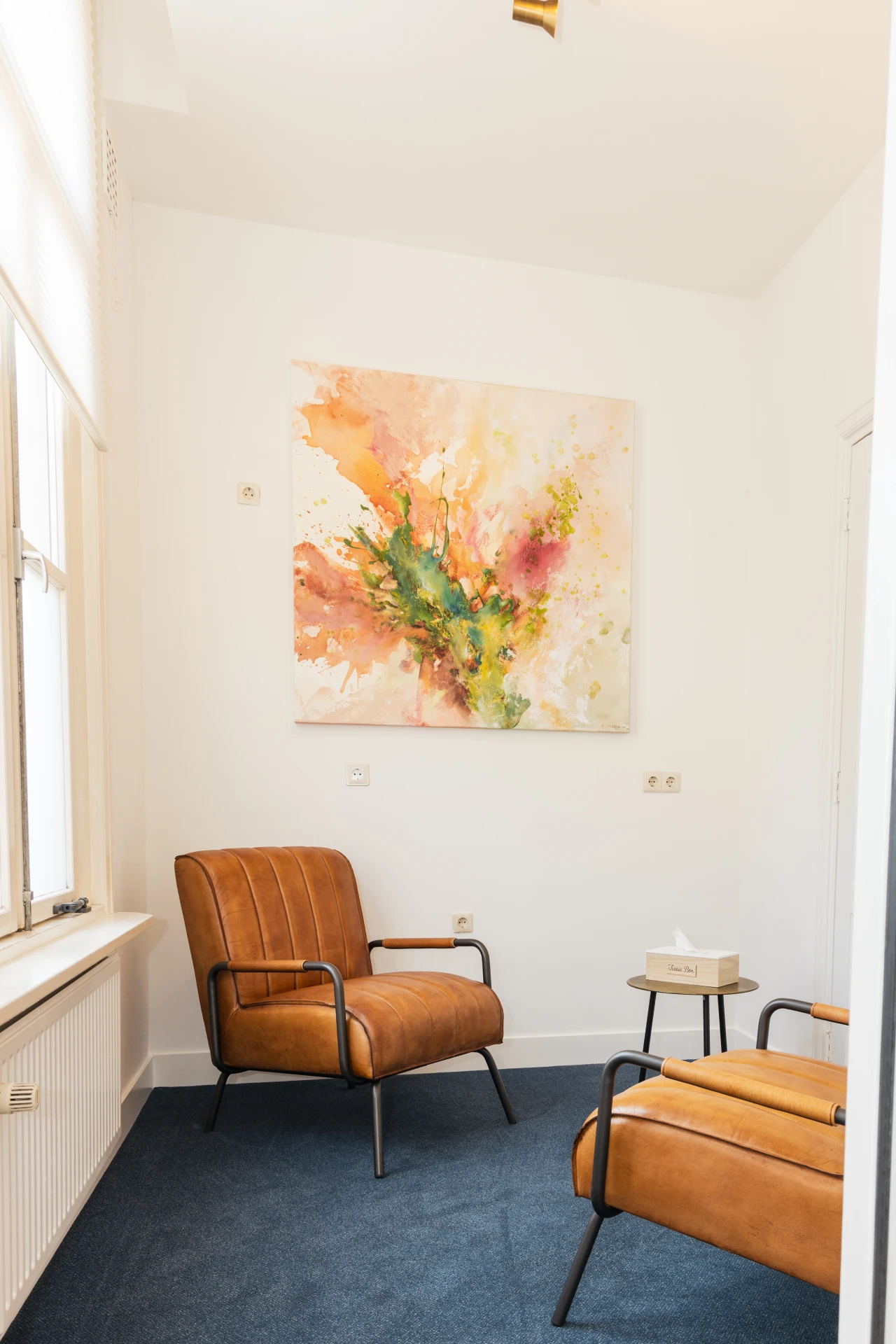 Behandelkamer van CACN Verslavingszorg met licht interieur, schilderij en 2 leren fauteuils.