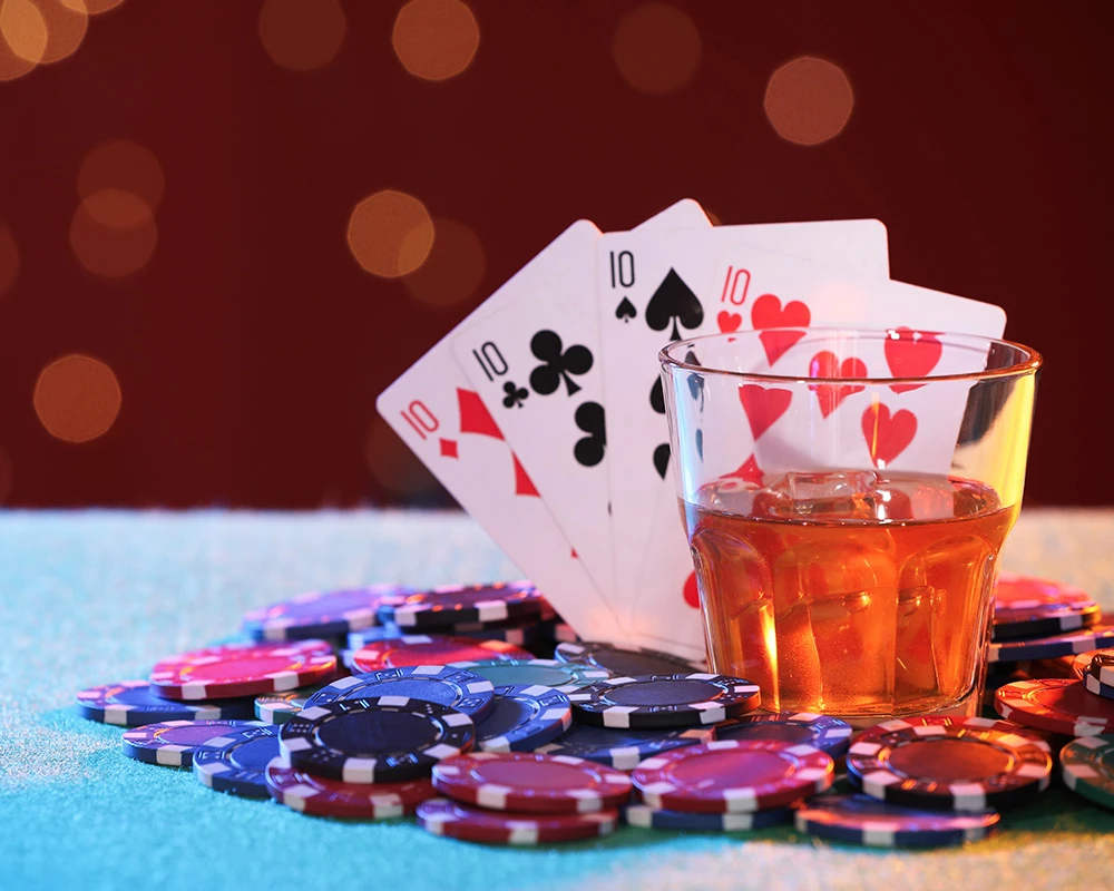 Glas alcohol, speelkaarten en fiches liggen op tafel tijdens een gokspel. De afbeelding verwijst naar de invloed van alcohol op impulsief gokgedrag.