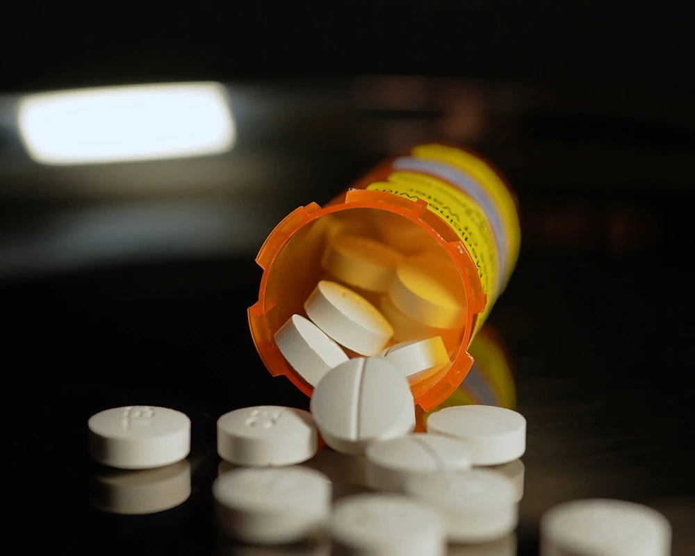 Medicijnpotje met witte pillen ligt omgevallen op een donkere ondergrond. De afbeelding past bij afhankelijkheid en de risico’s van een oxycodon verslaving.