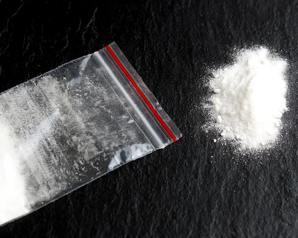 Zakje met wit poeder op een donkere ondergrond. De afbeelding past bij cross addiction, waarbij iemand meerdere middelen of verslavingen afwisselend gebruikt.