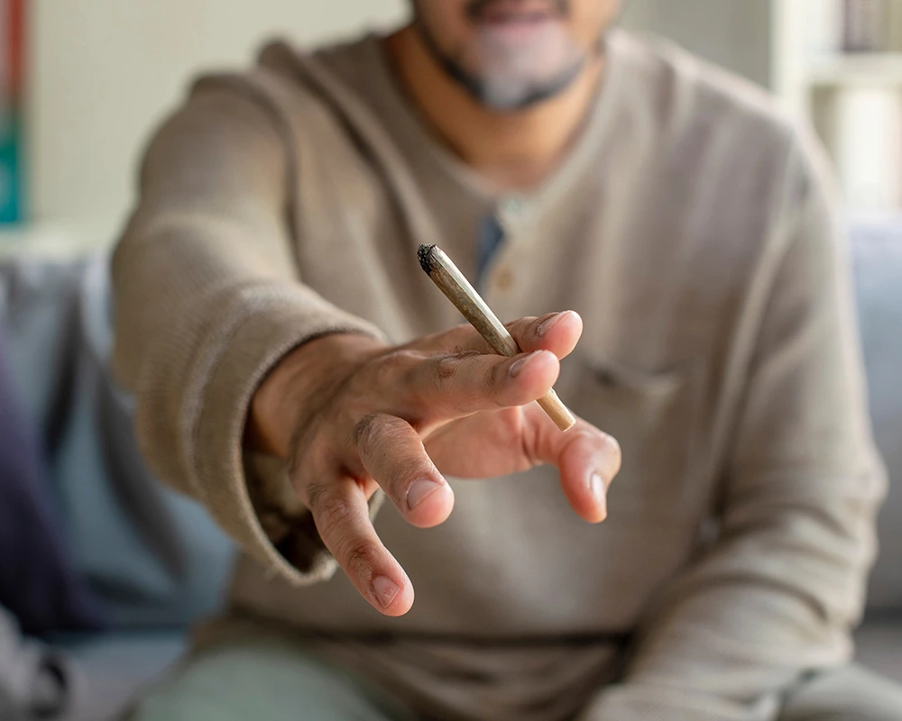 Een man houdt een joint vast in zijn hand. De afbeelding laat cannabisgebruik zien in relatie tot gokken en blowen en de mogelijke gevolgen van verslavingsgedrag.