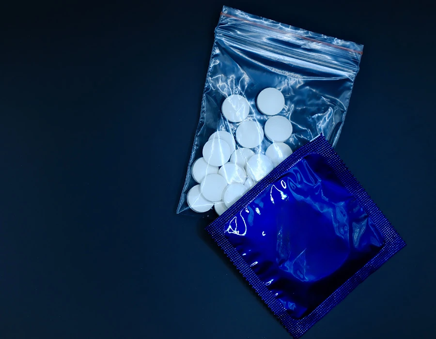 Witte pillen en een verpakt condoom op een donkere achtergrond.