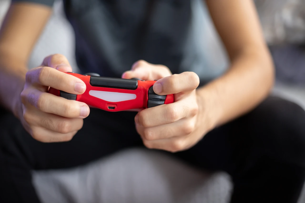 Handen houden een rode gamecontroller vast en voeden een gameverslaving. 