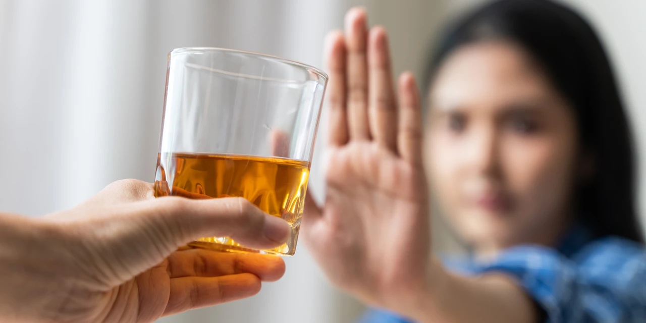 Een vrouw houdt haar hand op terwijl zij een glas alcohol weigert tijdens herstel.