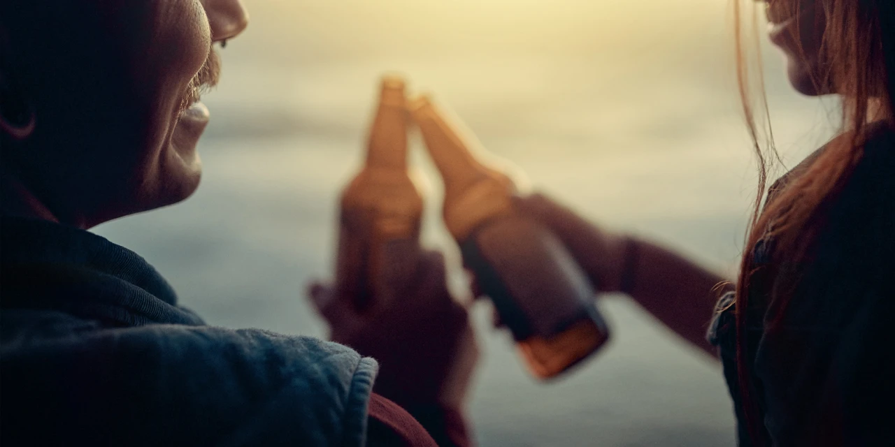 Twee mensen proosten met bierflesjes tijdens een sociaal moment in de buitenlucht.