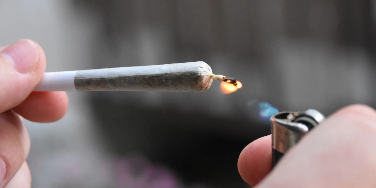 Close-up van een joint die met een aansteker wordt aangestoken terwijl iemand deze vasthoudt.