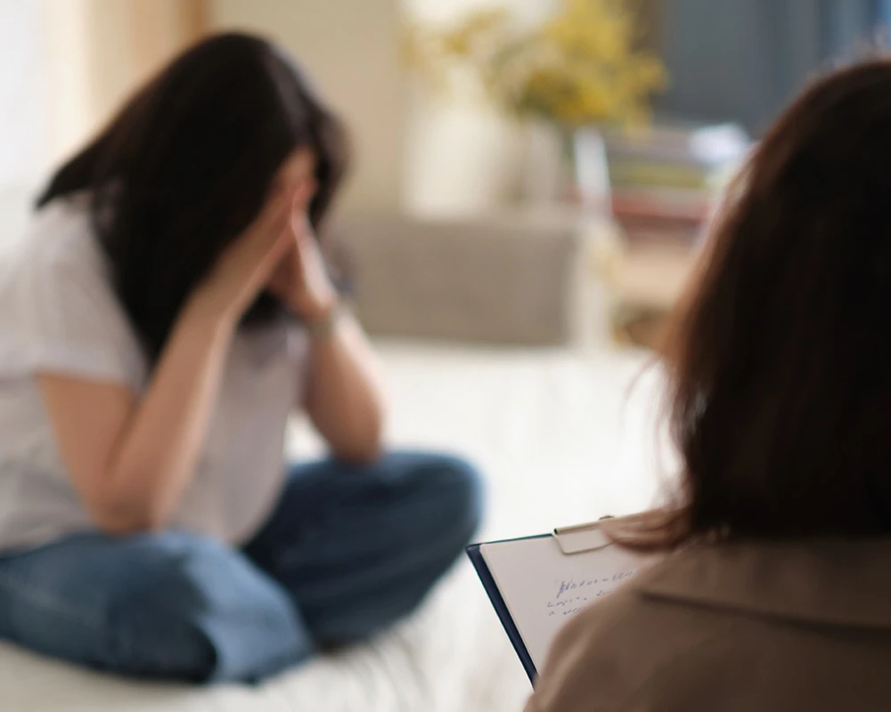 Iemand zit emotioneel tegenover een behandelaar tijdens een gesprek. De afbeelding verwijst naar mentale klachten en situaties die kunnen ontstaan bij een gedragsverslaving.