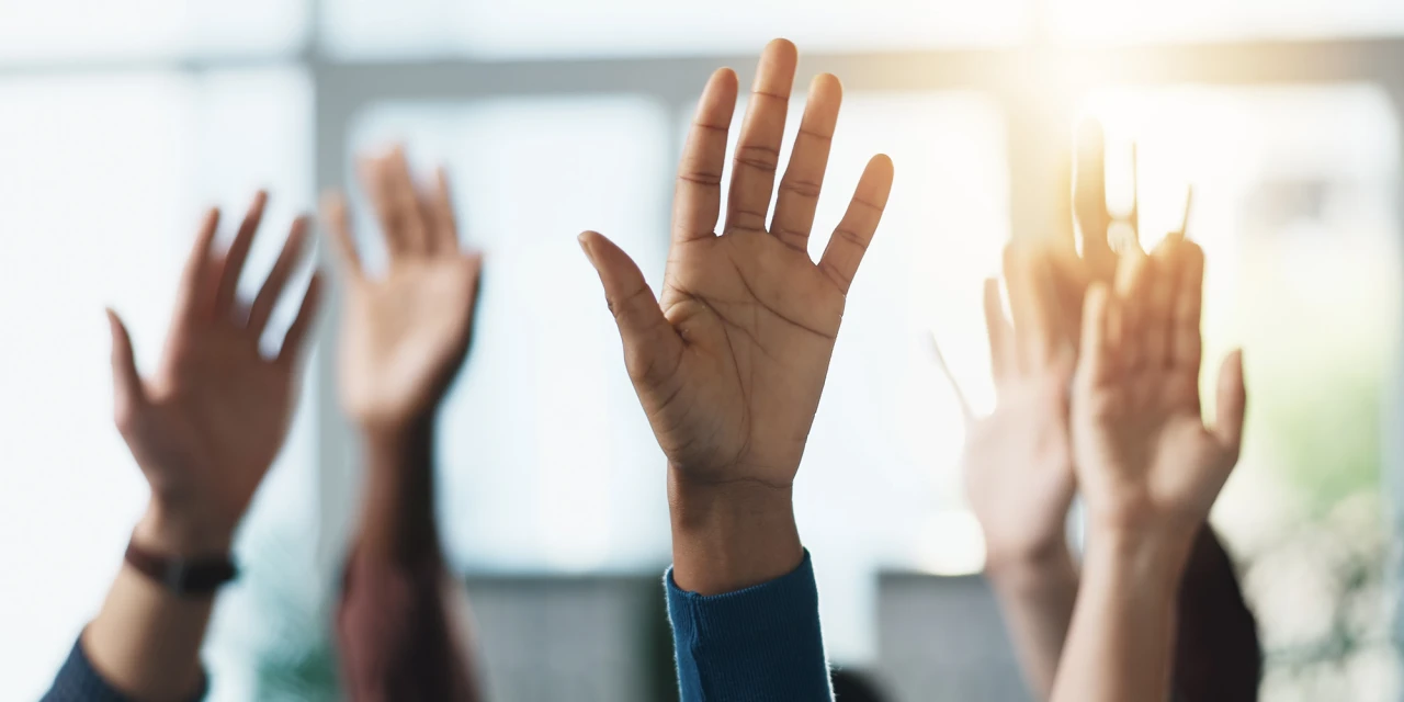 Meerdere mensen steken hun hand op tijdens een informatiesessie binnen de verslavingszorg om vragen te stellen en actief deel te nemen.
