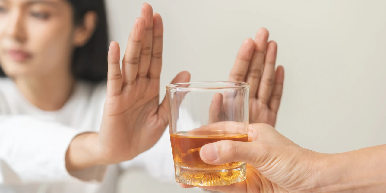 Een persoon houdt beide handen omhoog om een glas alcohol te weigeren.