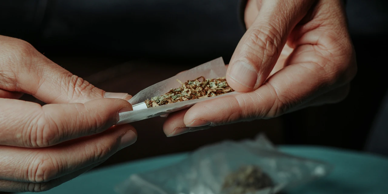 Iemand draait een joint met cannabis en tabak in vloei met beide handen.