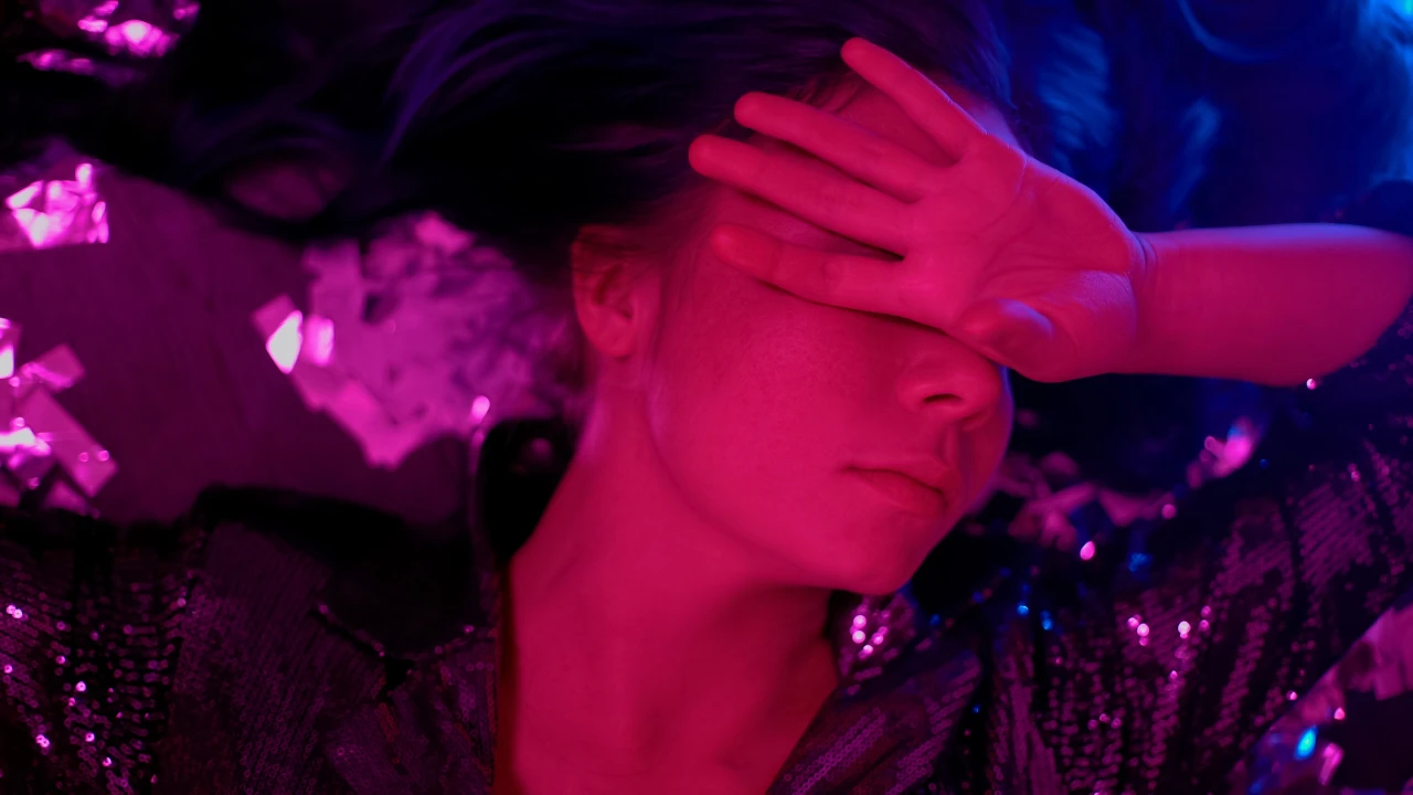 vrouw-in-club-met-XTC-verslaving Vrouw met XTC-verslaving staat in roze clubverlichting en houdt hand voor gezicht.