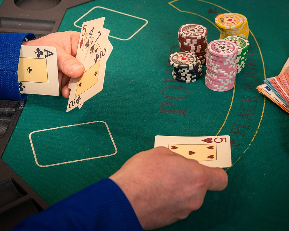 Iemand speelt een kaartspel aan een speeltafel met fiches en speelkaarten in beeld. De afbeelding verwijst naar gokken en gedrag dat kan passen bij een gokverslaving.
