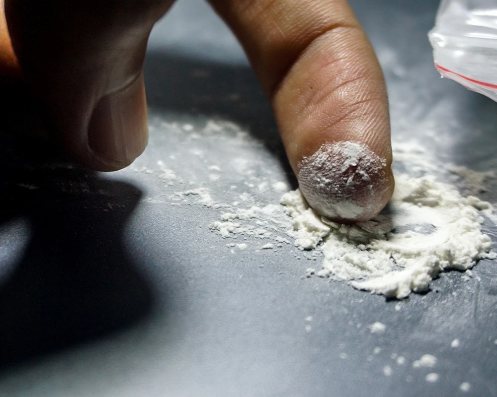 Vinger raakt wit ketaminepoeder aan op een donkere ondergrond. De afbeelding verwijst naar risicovol ketaminegebruik en de kans op een ketamine overdosis.