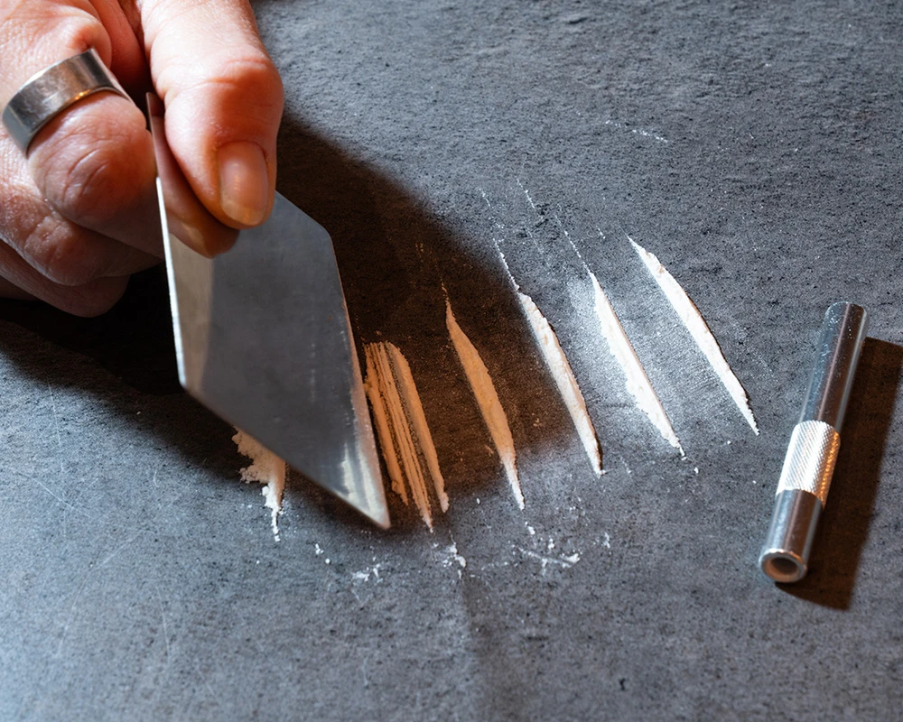 Witte speedlijnen worden klaargemaakt op een donkere ondergrond naast een snuifbuisje. De afbeelding past bij informatie over speedgebruik, speed en ADHD.