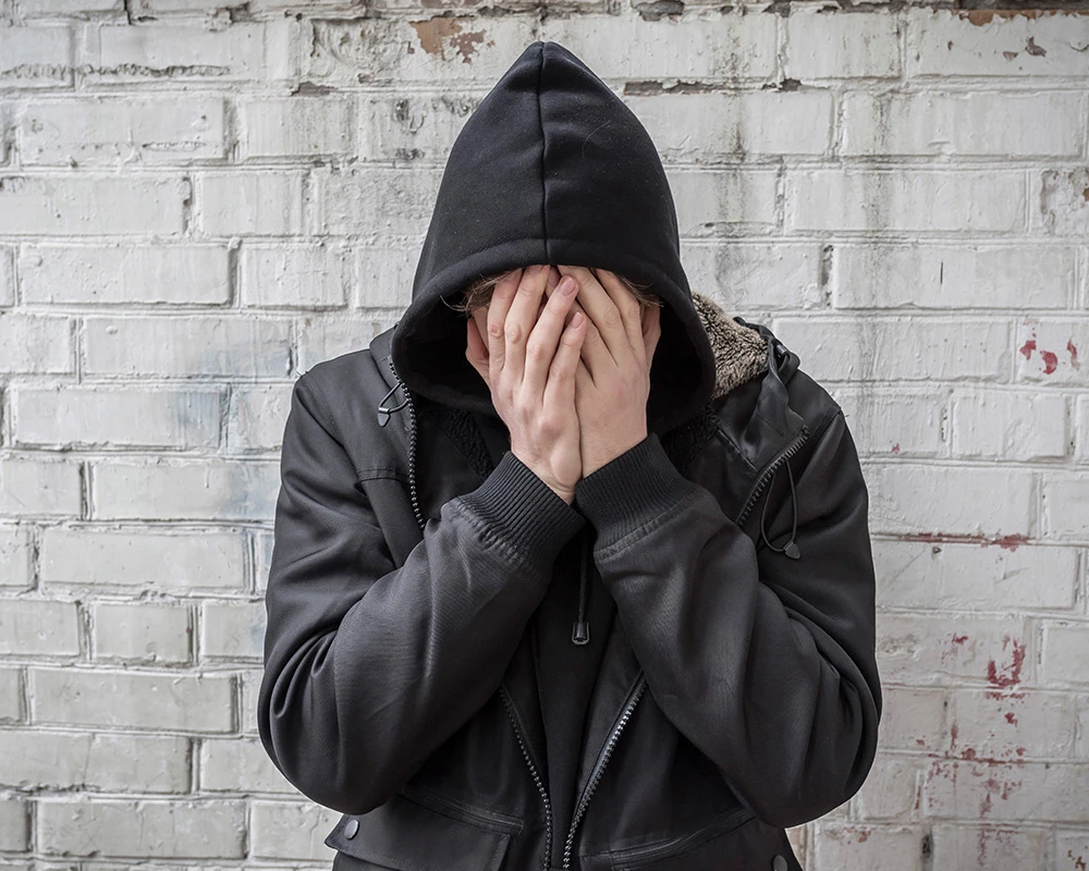 Persoon met hoodie zit met handen voor het gezicht tegen een muur. De afbeelding past bij de mentale en lichamelijke klachten die kunnen ontstaan tijdens cold turkey afkicken.