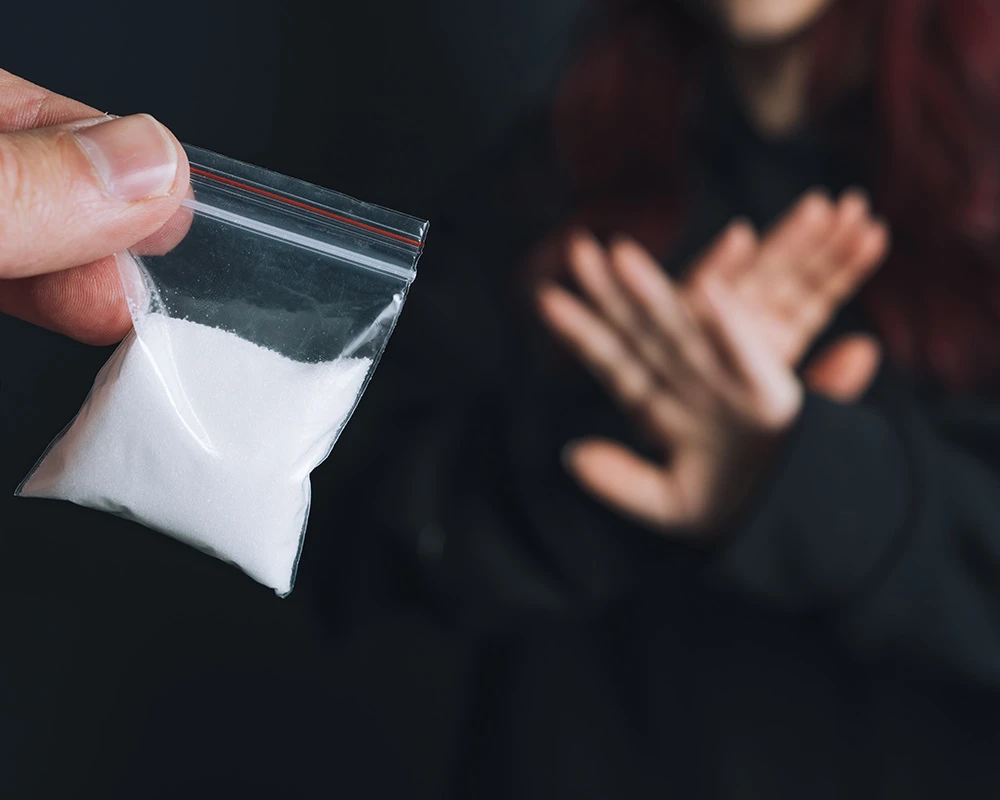 Persoon houdt afwerend zijn handen omhoog naast alcohol, pillen en drugsattributen. De afbeelding past bij stoppen met middelengebruik en het proces van afkicken.