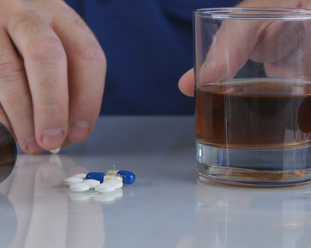 Een hand pakt medicatie naast een glas alcohol. De afbeelding toont gecombineerd gebruik van oxazepam en alcohol en de mogelijke risico’s daarvan.
