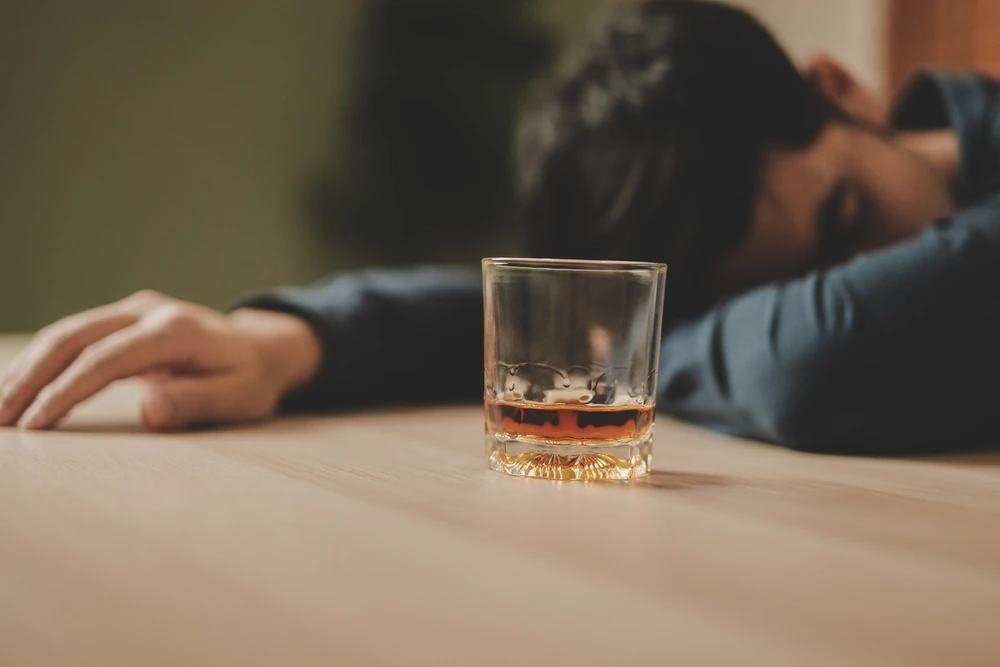 man-met-hoofd-op-tafel-bij-glas-alcohol Man ligt met zijn hoofd op tafel te slapen naast een bijna leeg glas alcohol.