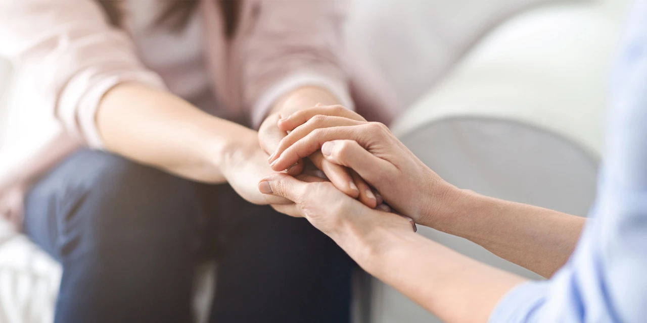Zorgprofessional houdt hand vast van cliënt tijdens steunend gesprek over mentale gezondheid.