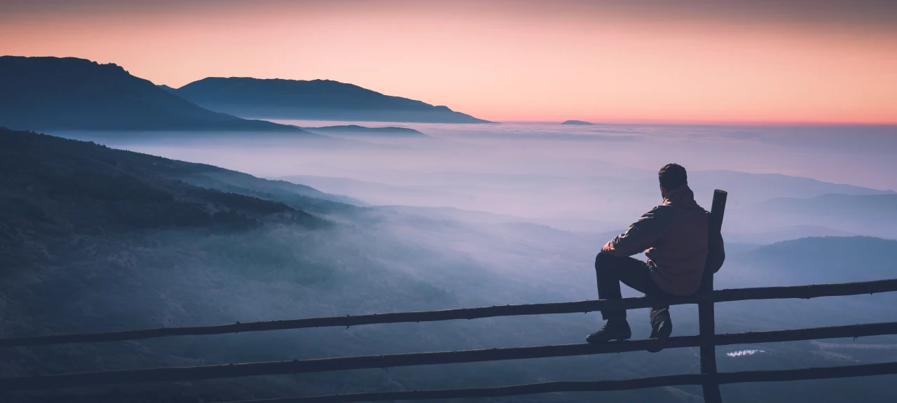 Man zit op hek en kijkt naar mistige bergen die het vage effect van ketamineverslaving symboliseren.