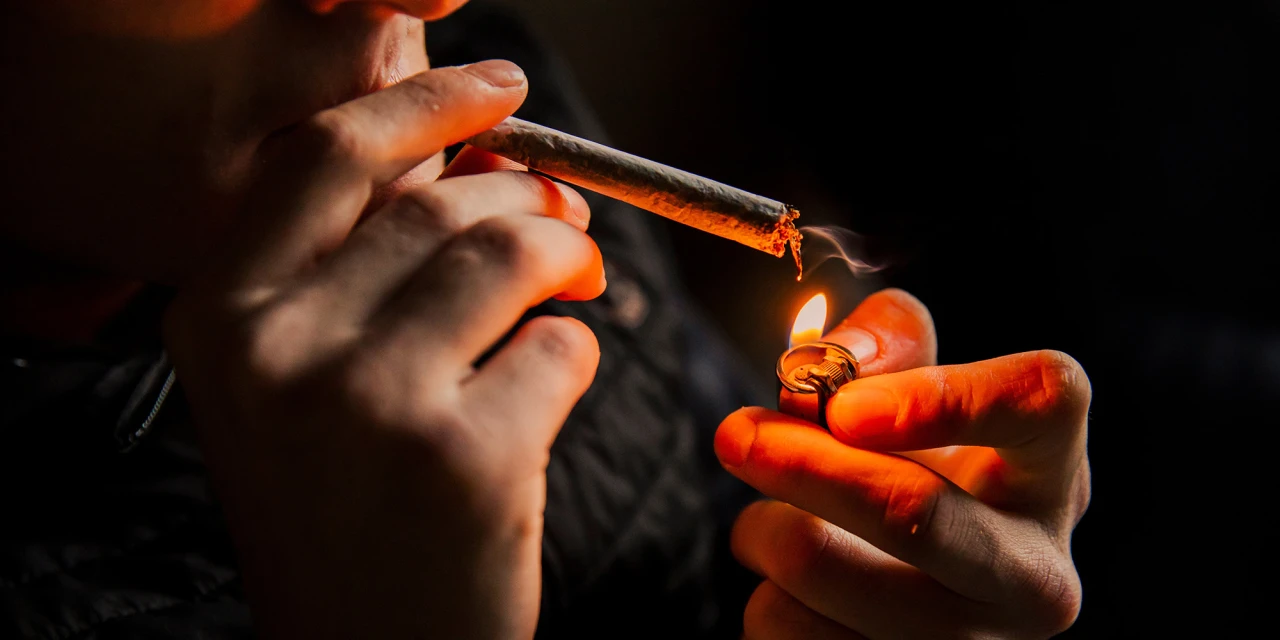 Iemand steekt een joint aan met een aansteker in een donkere omgeving.