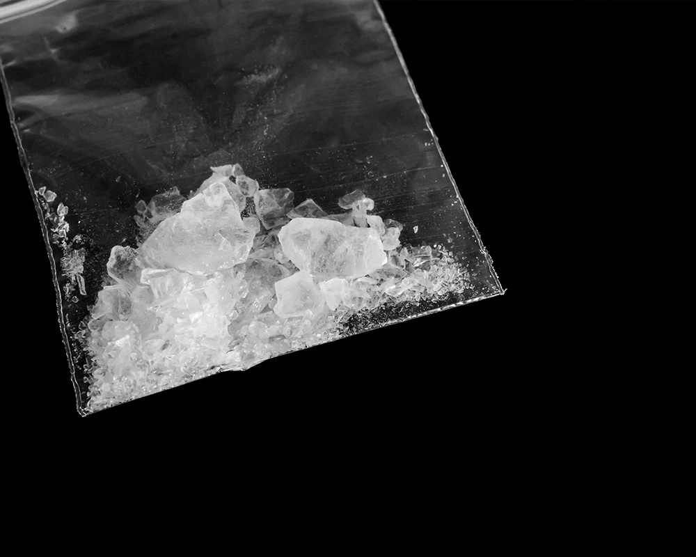 Plastic zakje met witte speedkristallen op een zwarte achtergrond. De afbeelding verwijst naar drugsgebruik en informatie over wat is speed.
