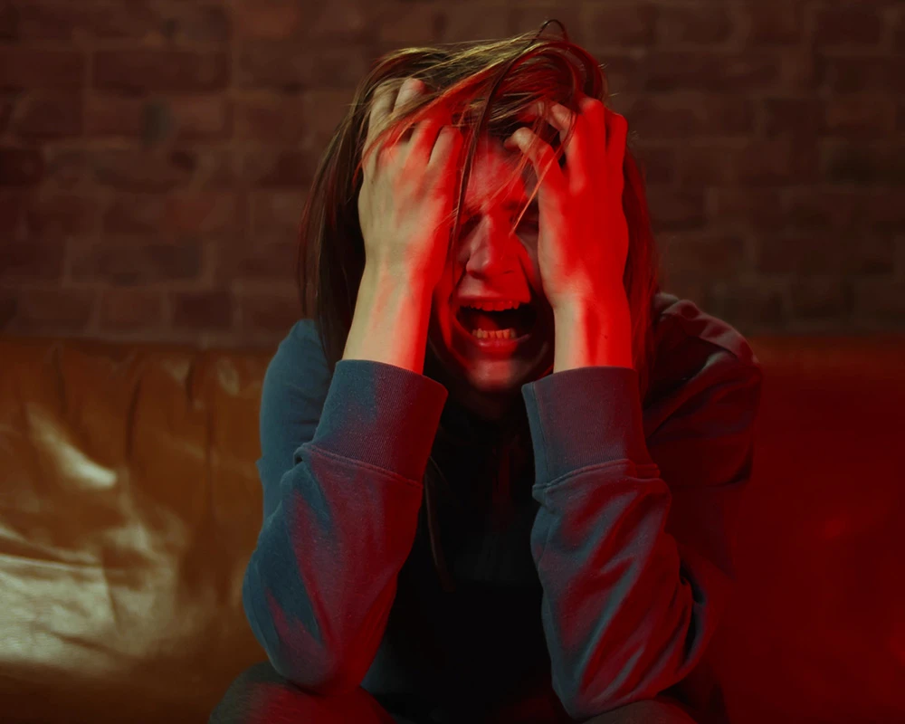 Persoon zit angstig en overstuur op een bank met handen in het haar. De afbeelding hoort bij informatie over mentale afkickverschijnselen en emotionele onrust tijdens herstel.