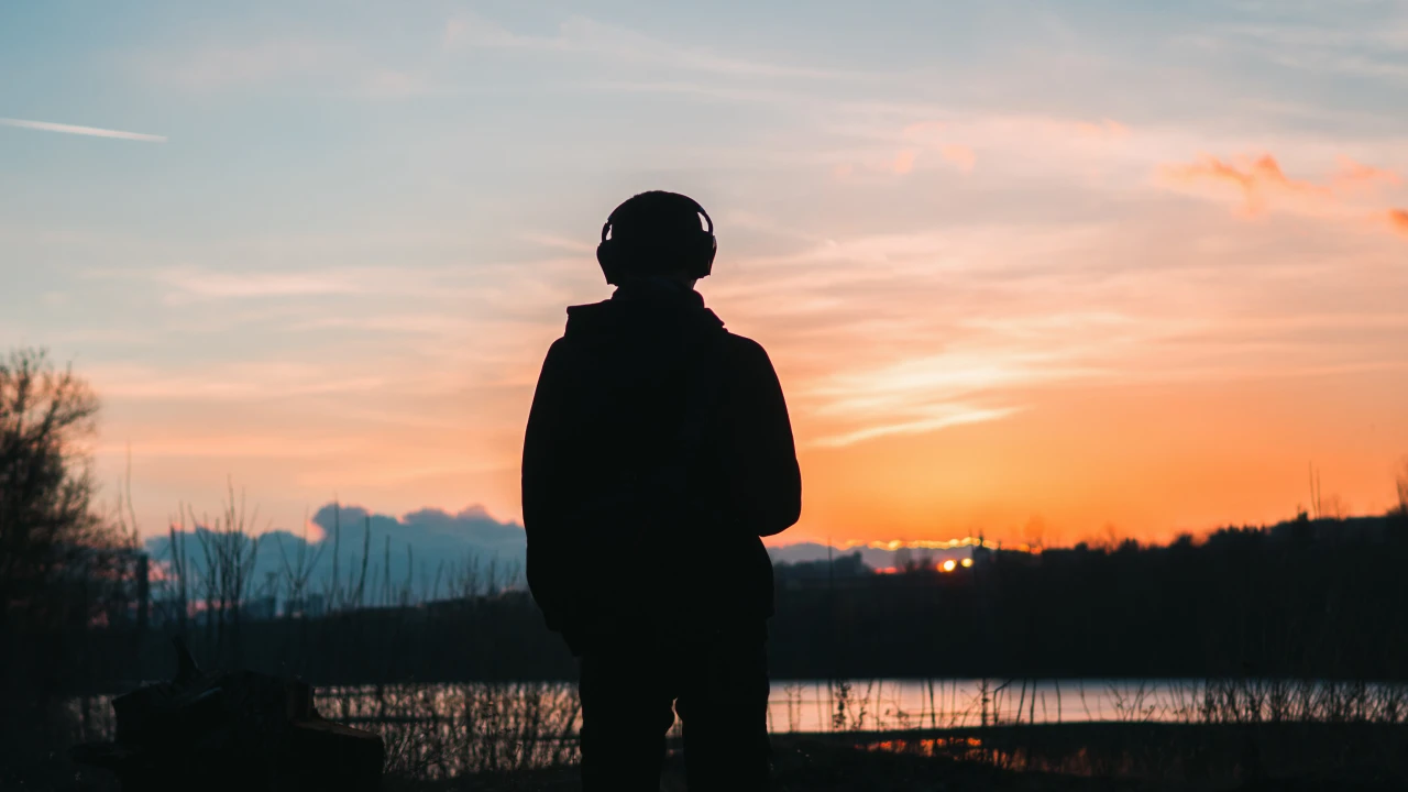 persoon-met-koptelefoon-bij-ondergaande-zon Persoon staat in bosachtige gebied aan water en is eenzaam doordat hij door blowen depressief is.