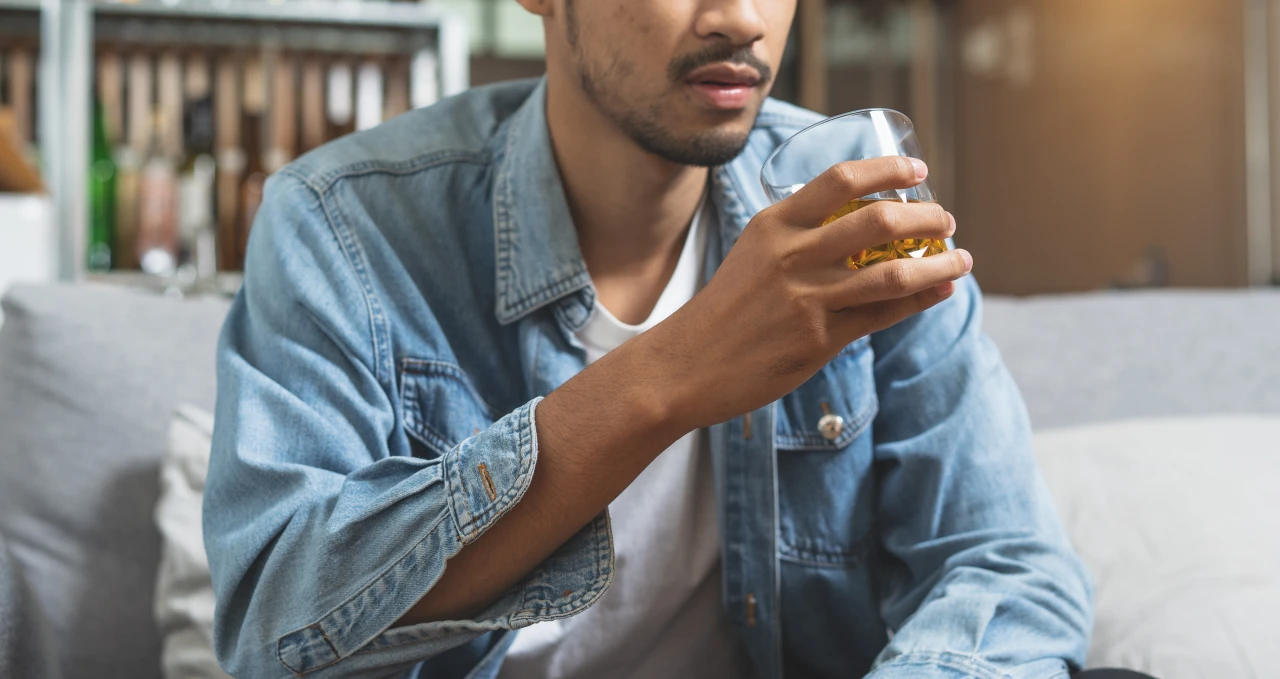 Man zit met glas whiskey in de hand op bank en lijdt aan alcoholabusus.