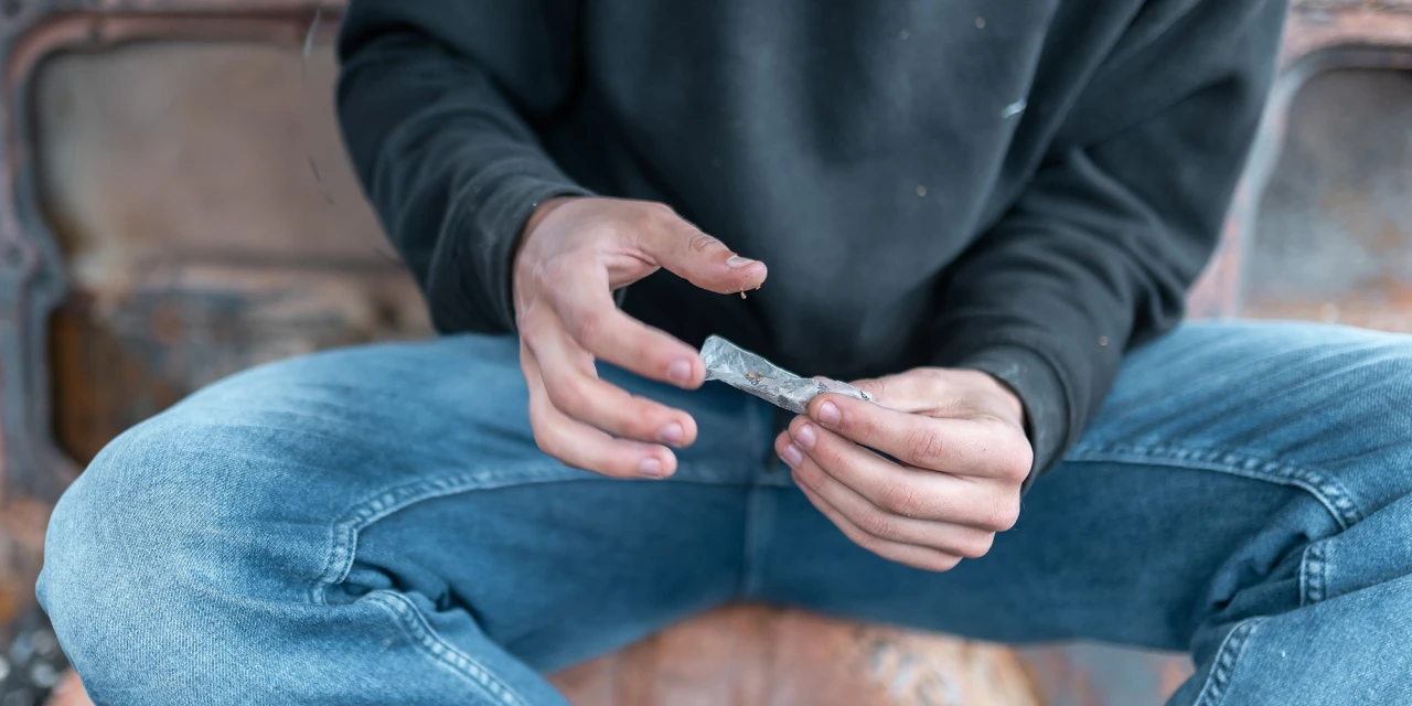 Persoon draait een joint terwijl hij op de grond zit, passend bij dagelijks blowen en cannabisgebruik.