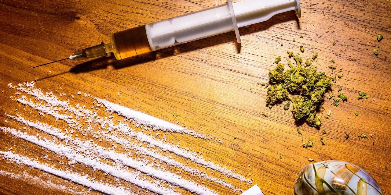 Cocaïnelijnen, wiet en drugsaccessoires op een houten tafel, passend bij gecombineerd gebruik van cocaïne en cannabis.