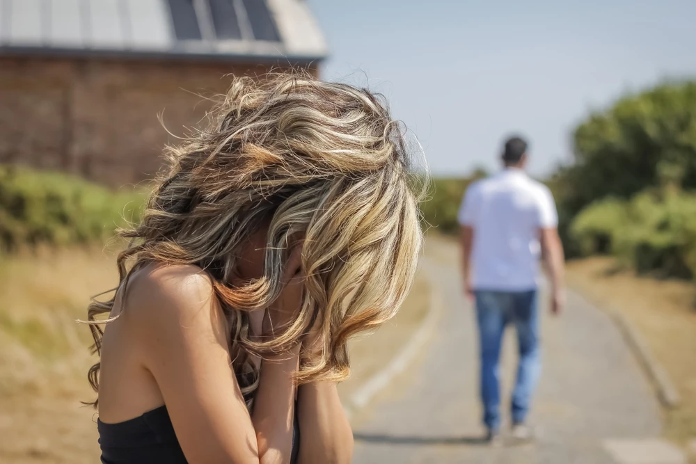 Vrouw verbergt haar hoofd in haar handen terwijl haar man bij haar wegloopt als gevolg van het blowen. 