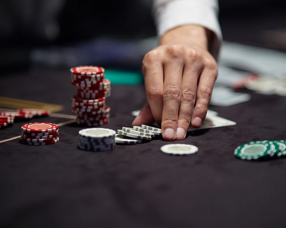 Iemand schuift fiches over een pokertafel tijdens een kansspel. De afbeelding verwijst naar gokken en gedrag dat kan passen bij een gokverslaving.