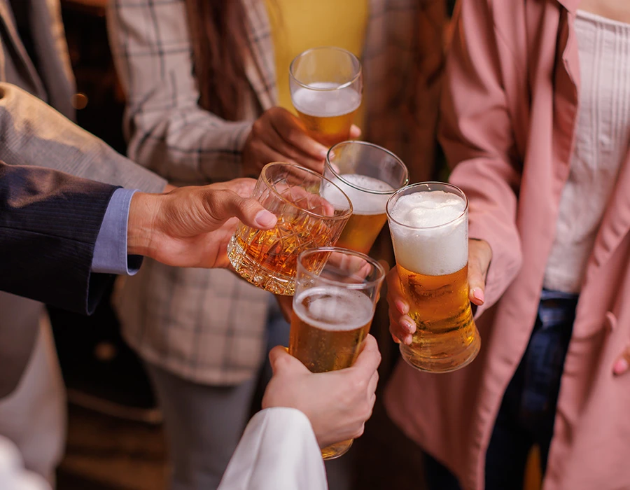 Meerdere personen proosten met bier en sterke drank tijdens een sociale bijeenkomst, passend bij alcoholgebruik en bingedrinken.