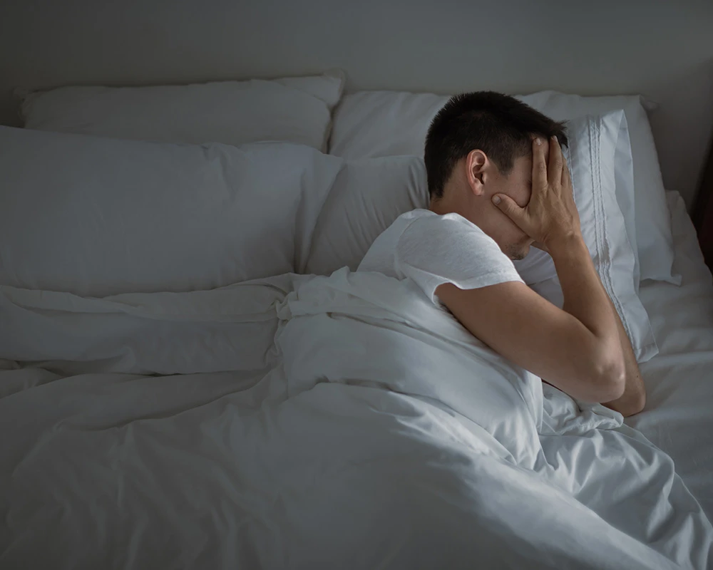 Een man zit wakker in bed met zijn hand voor zijn gezicht. De afbeelding toont stress, slapeloosheid en mentale onrust rondom een plafonddienst.
