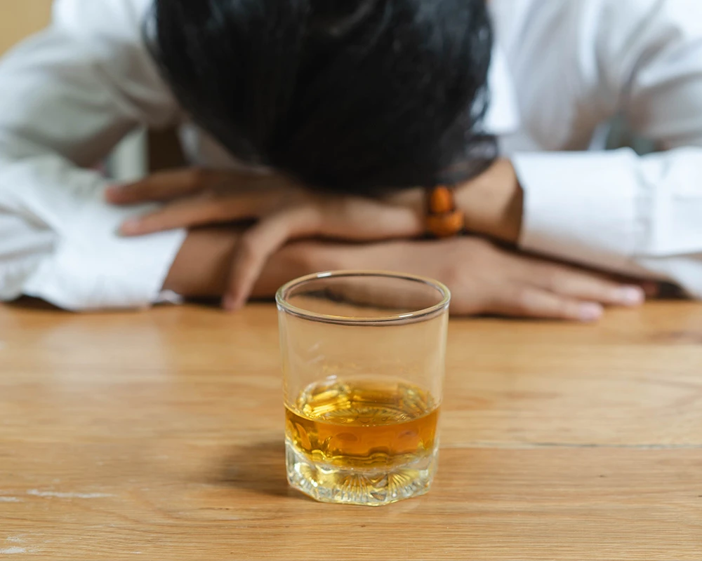 Persoon met glas alcohol op tafel als beeld van dipsomanie en uitputting.