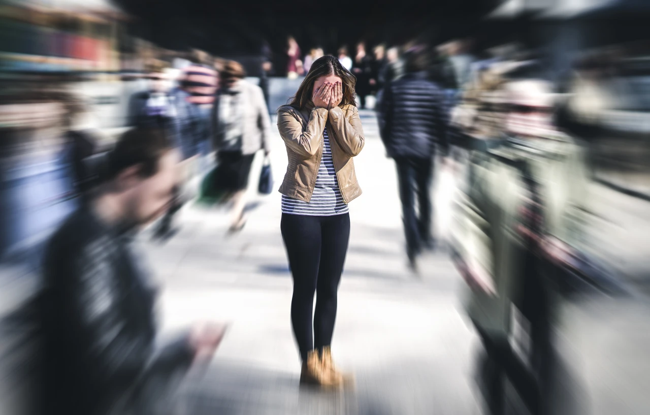 vrouw-staat-tussen-voorbijgangers-met-handen-voor haar-gezicht Vrouw met handen voor haar gezicht staat tussen voorbijgangers.