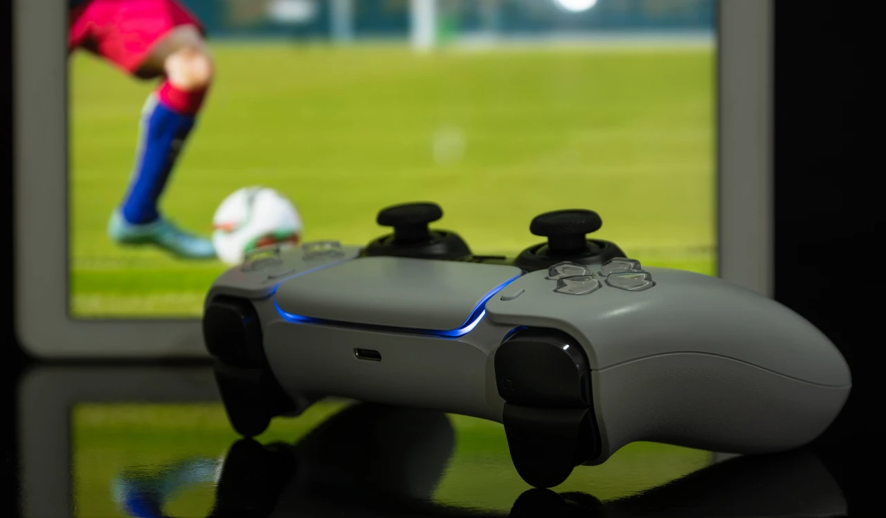Game-controller-met-beeldscherm-op-achtergrond-met voetbalspel Game-controller ligt op tafel met op achtergrond beeldscherm met FIFA.