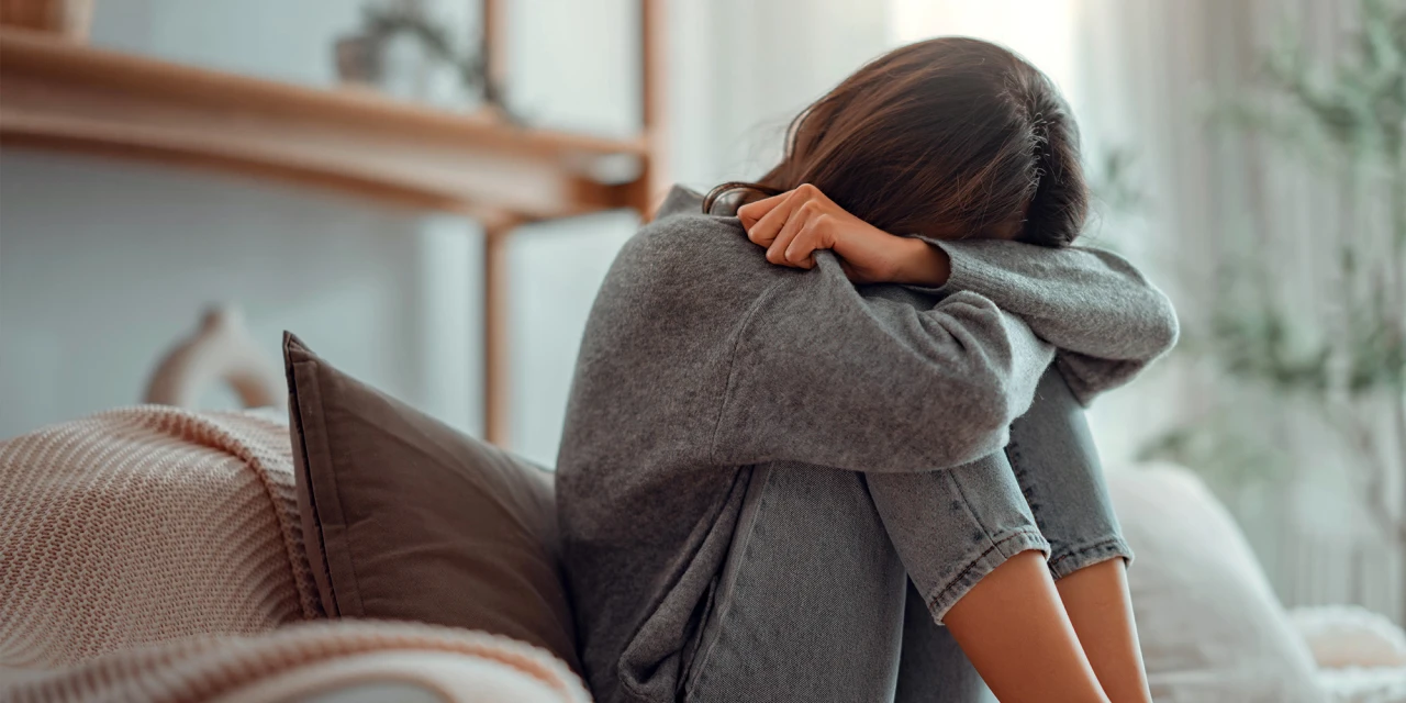 Een vrouw zit verdrietig op de bank met haar hoofd op haar armen tijdens een moeilijk moment.