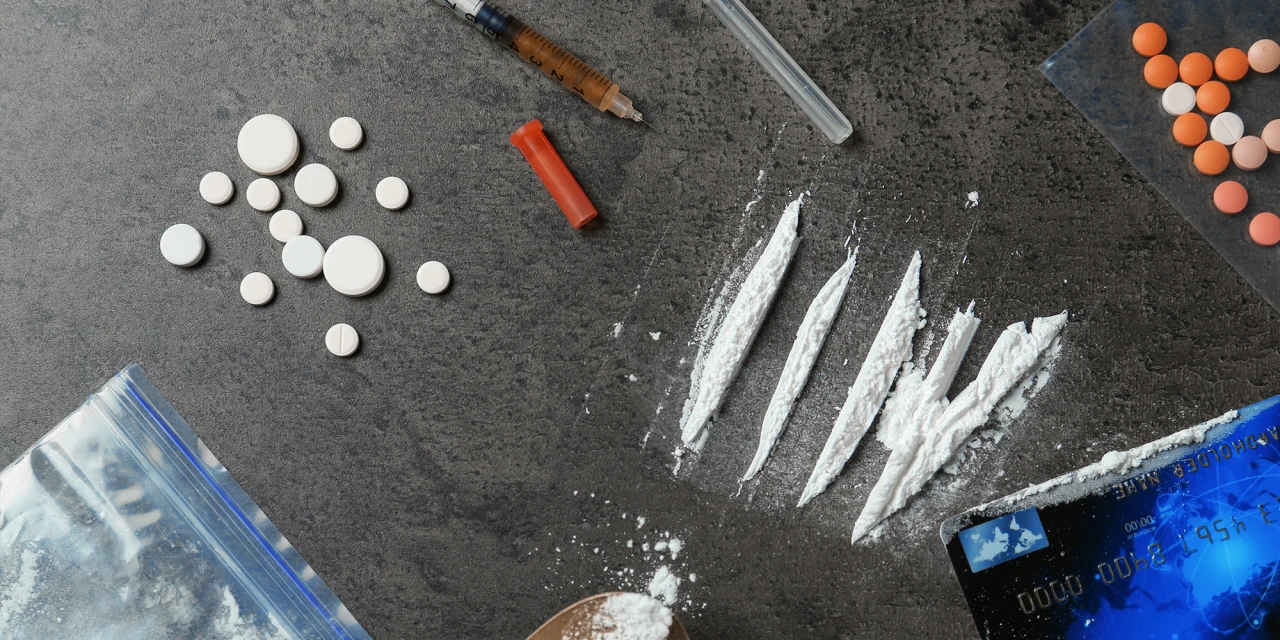 Cocaïnelijnen, pillen en drugsgerelateerde spullen op tafel, passend bij de risico’s en verslavendheid van coke.