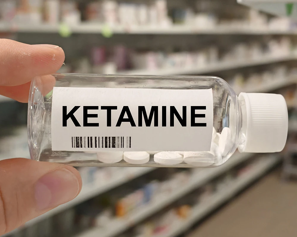 Persoon houdt een flesje met het label ketamine vast in een apotheekomgeving. De afbeelding verwijst naar ketaminegebruik en de mogelijke risico’s van misbruik.