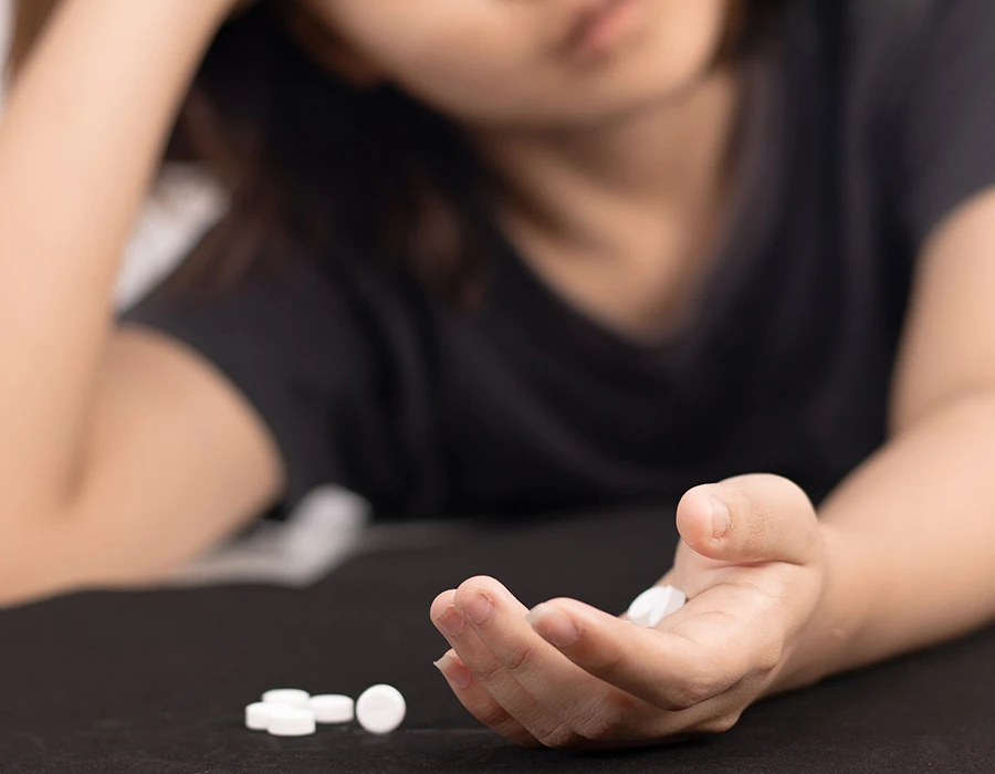 Persoon kijkt uitgeput naar pillen op tafel, wat de mentale en emotionele impact van een verslaving laat zien.