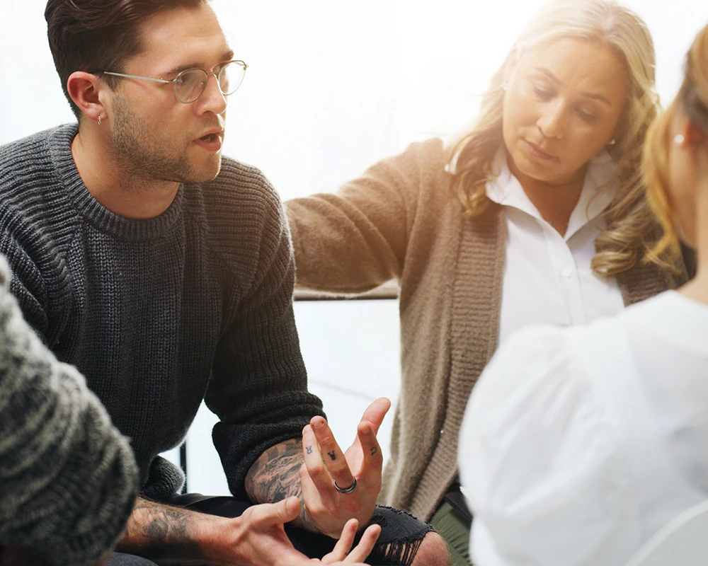 Een groep mensen voert een open gesprek tijdens een therapiesessie binnen de verslavingszorg met aandacht voor persoonlijke begeleiding.