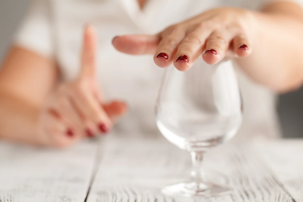 vrouw-bedekt-wijnglas-met-hand Vrouw bedekt wijnglas met hand en steekt vinger op omdat ze wil stoppen met drinken.