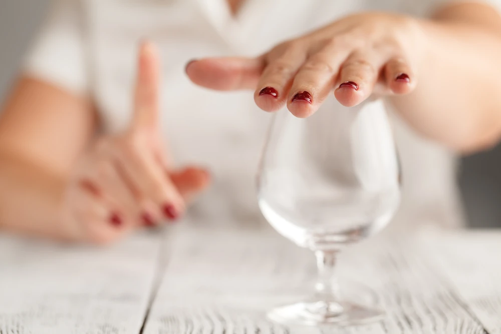 Vrouw bedekt wijnglas met hand en steekt vinger op omdat ze wil stoppen met drinken.