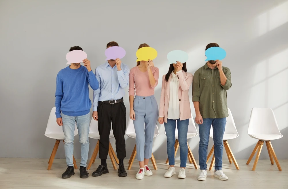 5-mensen-staan-naast-elkaar-met-verborgen-gezicht 5 mensen houden vel papier in de vorm van een praatwolkje voor het gezicht.