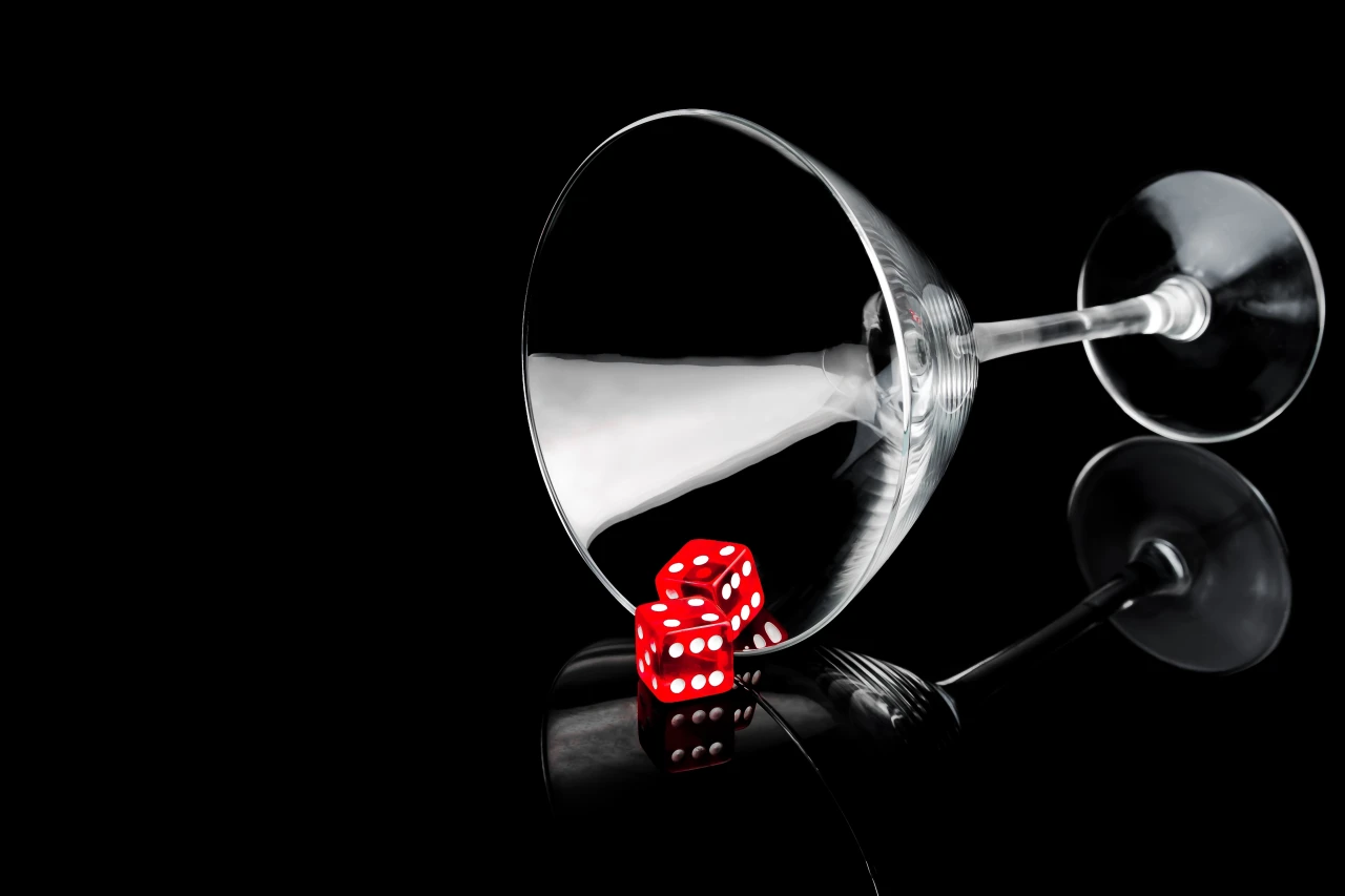 Gokken en alcohol uitgebeeld door omgevallen en leeg cocktailglas met 2 rode dobbelstenen.