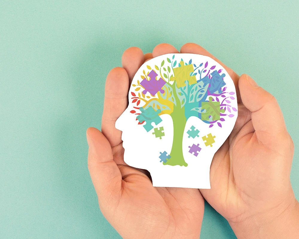 Illustratie van een hoofd met een kleurrijke boom en puzzelstukken als symbool voor ADHD en mentale gezondheid. De afbeelding past bij informatie over ADHD en verslaving.