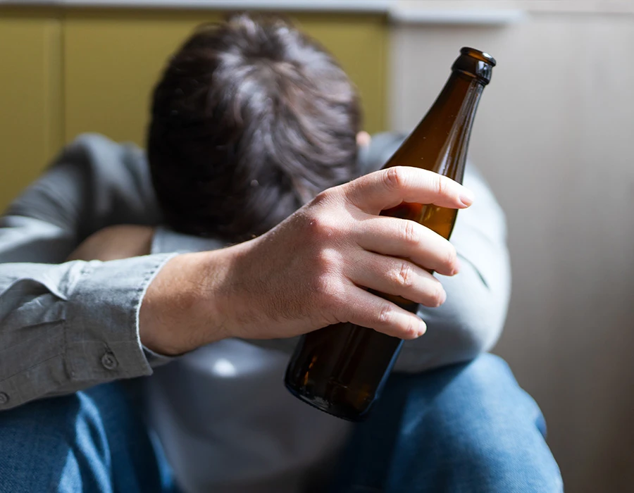 Een persoon zit somber met een bierfles in de hand, passend bij problematisch alcoholgebruik en mentale klachten.