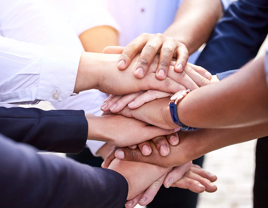Een groep mensen legt handen op elkaar als teken van vertrouwen, steun en gezamenlijke inzet tijdens een hersteltraject binnen de verslavingszorg.